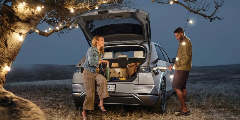 Two people standing near an open car trunk outdoors at dusk