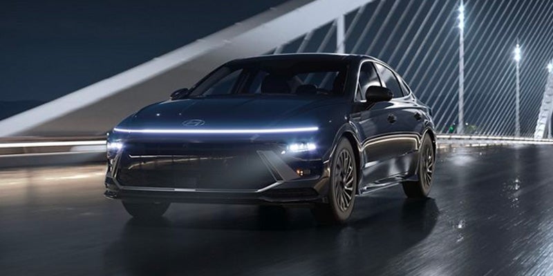 Dark-colored Hyundai Sonata driving at night on a wet bridge with illuminated architectural cables