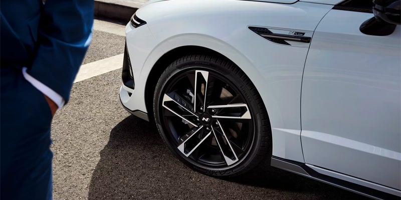 white car’s front wheel featuring a black and silver alloy rim parked on a paved road
