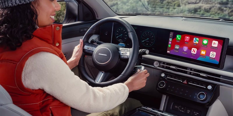 Woman in a fuzzy white sweater and orange vest holding a smart key in a modern car with a large touchscreen.