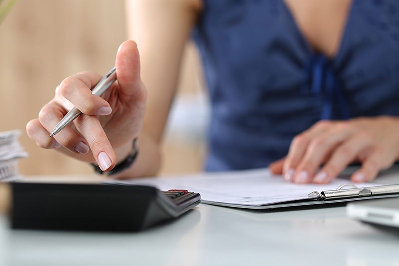 Close-up of a person using a calculator and holding a pen while reviewing documents on a desk